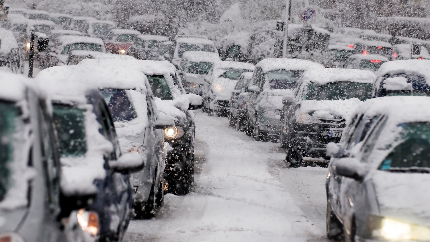 Filas de coches, cubiertos de nieve, esperan en carreteras nevadas.